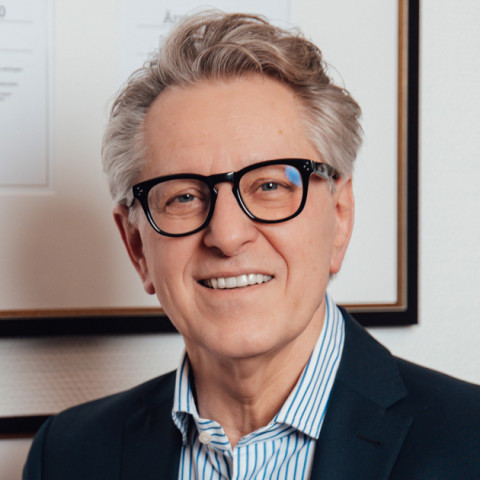 Porträt von Dr. med. Marian Stefan Mackowski in seiner Praxis, mit Brille, dunklem Sakko und gestreiftem Hemd